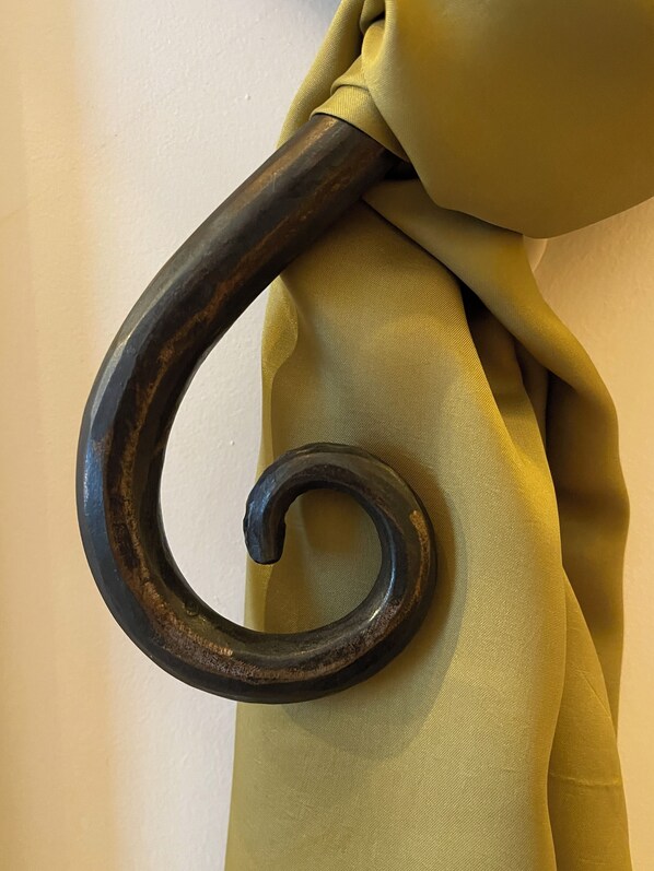 A close-up of a dark, ornate metal hook attached to a fabric.