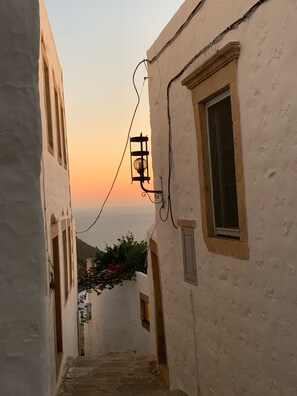 A narrow street with white buildings, a street lamp, and a view of the sea at sunset. - Chora - old house - sea / Chora - nice antic house - sea view (Patmos)