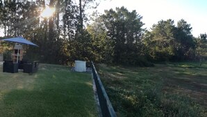 A stone house with a red roof, a patio with chairs and a table, and a view of a grassy field and trees.