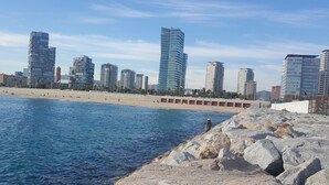 A coastal cityscape with modern high-rise buildings, a sandy beach, and rocky terrain.