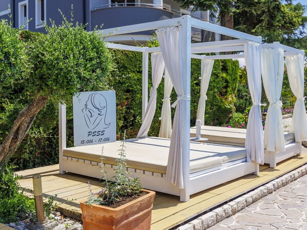 A white outdoor bed with a canopy, a sign with a woman's silhouette, and a time schedule.