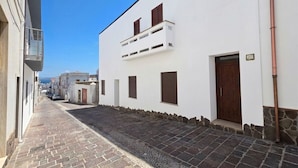 Une rue étroite bordée de bâtiments blancs, avec un pavé de pierre et un ciel d’un bleu limpide.