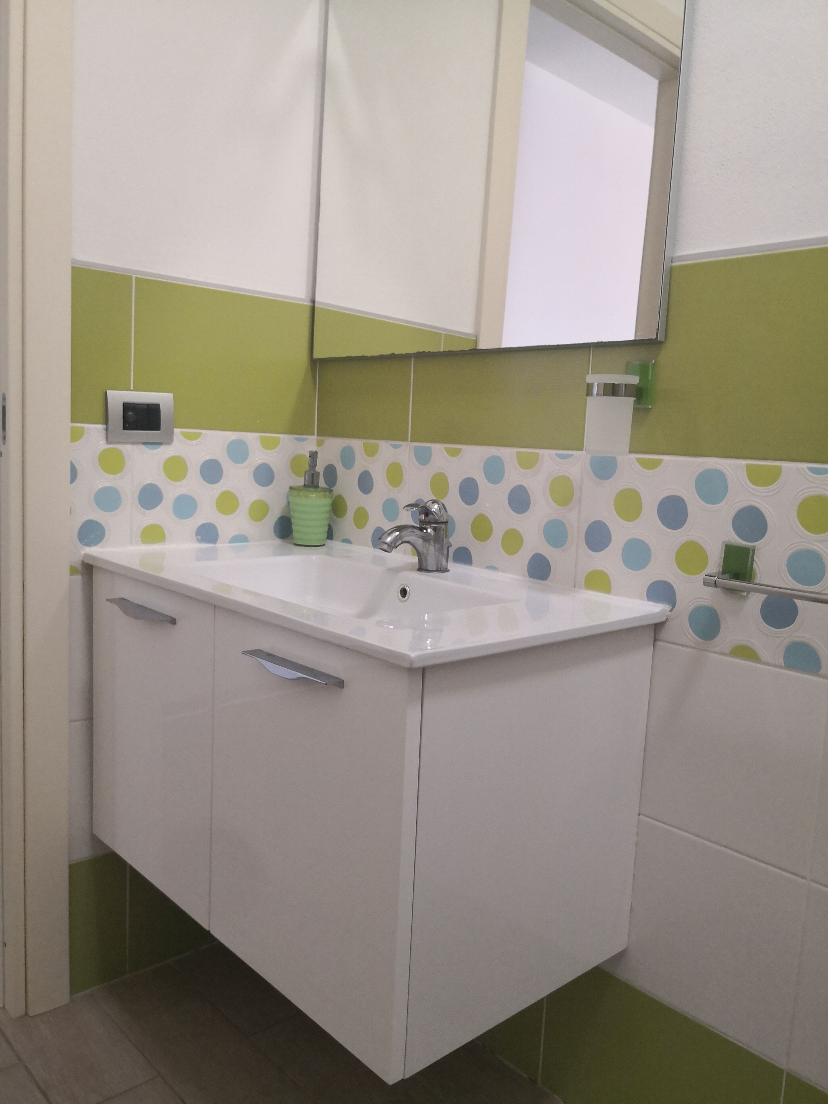 Une salle de bain avec un lavabo blanc, des carreaux à pois verts et bleus et un miroir au-dessus du lavabo.