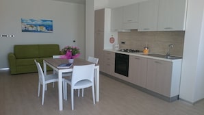 Une cuisine compacte dotée d’appareils électroménagers modernes, un coin repas avec une table et des chaises, et un canapé vert dans un petit salon.