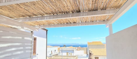 Un balcó amb sostre de bambú, parets blanques i una taula amb mantell de taula amb estel de mar.