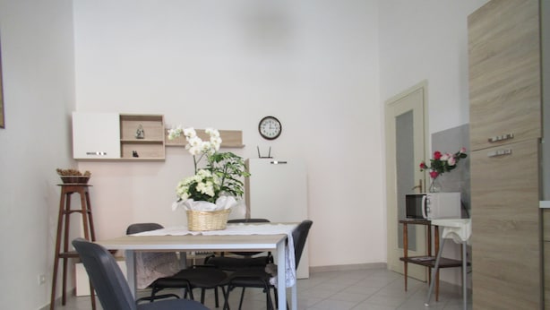 A compact kitchen with a dining area, featuring a microwave, a clock, and a small refrigerator. - Holiday Monferrato - LE GINESTRE - WI-FI AND PARKING FREE (Tonco)