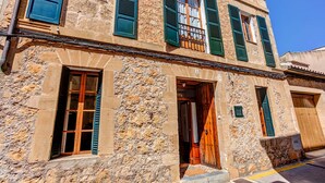 Un bâtiment en pierre avec des volets verts, une porte en bois et un balcon bien visible.