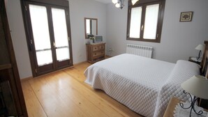 Ein Schlafzimmer mit einem großen Bett, Holzboden, einem Schminktisch, einem Spiegel und einem Fenster mit Vorhängen.