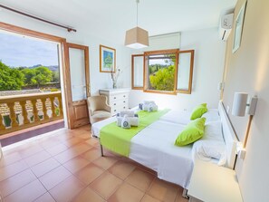A hotel room with a balcony, a bed with green pillows, a dresser, and a painting on the wall.