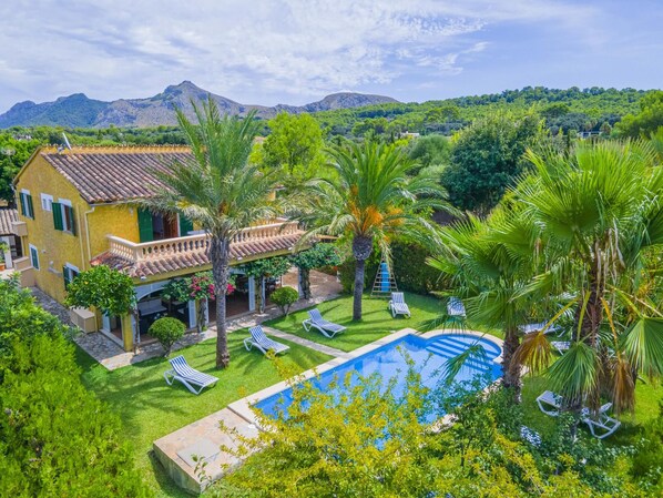 A villa with a swimming pool, surrounded by lush greenery and palm trees.