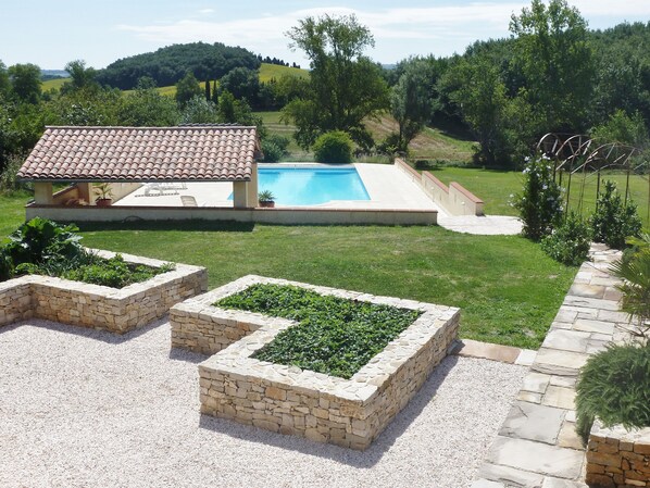 A villa with a swimming pool, stone planters, and a view of rolling hills.