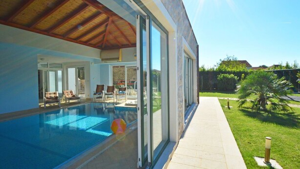 Una casa moderna con piscina, puertas de vidrio amplias y un césped bien cuidado.