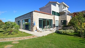 Una casa moderna de dos pisos con fachada de piedra, grandes ventanales y un césped bien cuidado.