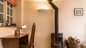 Une pièce chaleureuse avec un poêle à bois, un bureau avec une lampe, une chaise et un seau de bois de chauffage.