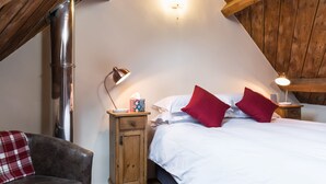 Une chambre avec un plafond en pente, un lit avec une literie blanche et des oreillers rouges, une table de chevet en bois avec une lampe, et une petite armoire.