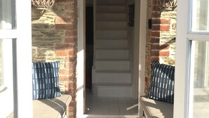 A covered outdoor seating area with a wooden floor, a brick wall, and a staircase leading to an upper level. - Waterside cottage in a  magical setting on the Salcombe Estuary (sleeps 6) (Kingsbridge)