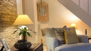 A cozy living room with a blue sofa, a lamp, a wicker side table, and a staircase. - Waterside cottage in a  magical setting on the Salcombe Estuary (sleeps 6) (Kingsbridge)