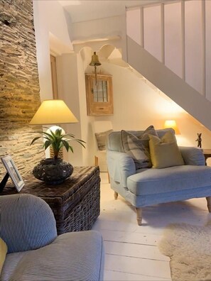 A cozy living room with a blue sofa, a lamp, a wicker side table, and a staircase. - Waterside cottage in a  magical setting on the Salcombe Estuary (sleeps 6) (Kingsbridge)
