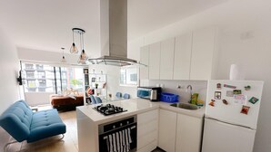 A modern kitchen with white cabinets, a central island with a stove, a sink, and a refrigerator adorned with magnets. - Exclusive, One Step Away from San Isidro (1302) (Lima)