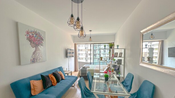 A modern living room with a blue sofa, glass coffee table, and teal chairs. A large mirror and a painting adorn the walls. - Exclusive, One Step Away from San Isidro (1302) (Lima)