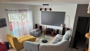 Un saló amb un sofà, una otomana i algunes cadires, un televisor de pantalla plana, altaveus i una taula de centre.