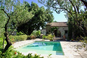 A stone pool surrounded by greenery, with a stone building in the background. - Villa Les Bouyssières - Fairytale Stone House, Pool, Enchanting Gardens & Views. (Ferrières-Les-Verreries)