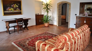 Uma sala de estar com sofá, mesa de jantar, cadeiras, planta em vaso e um quadro na parede.