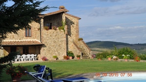 Um edifício de pedra com piscina, área de estar ao ar livre e vista para as colinas.