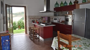 Cozinha com ilha central, mesa de jantar e vista para um jardim através de uma porta aberta.