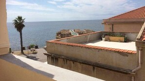 Eine Dachterrasse mit Blick auf das Meer, einer Palme und einem Gebäude mit Ziegeldach.