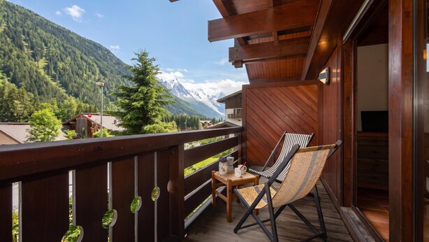 Un balcon en bois avec une chaise et une table, donnant sur un paysage montagneux.