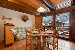 Un intérieur en bois avec une table à manger dressée pour deux personnes, un canapé et une fenêtre donnant sur un paysage enneigé.