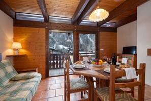 Un intérieur en bois avec une table à manger dressée pour deux personnes, un canapé et un téléviseur.