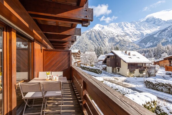 Ein Holzbalkon mit Tisch und Stühlen, der auf eine verschneite Berglandschaft blickt.