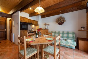 Eine gemütliche Küche mit Holzschränken, einem Esstisch für vier Personen und einem grün karierten Sofa.