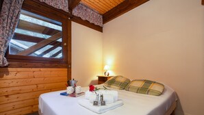 Un lit bien fait, avec une tablette contenant des articles de toilette, une lampe et une fenêtre dotée d’un plafond en bois.