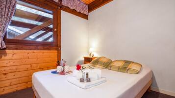Une chambre d’hôtel avec un plafond en bois, un lit recouvert d’une couette blanche, une table de chevet avec une lampe et une fenêtre avec des rideaux.
