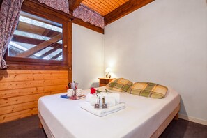 Une chambre d’hôtel avec un plafond en bois, un lit recouvert d’une couette blanche, une table de chevet avec une lampe et une fenêtre avec des rideaux.