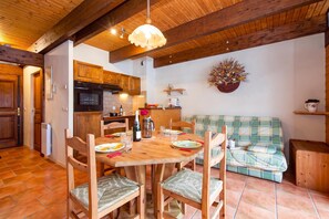 A wooden dining table with chairs, a kitchen area with wooden cabinets, and a plaid sofa. - Chalet Chantey Mourry6 Mountain-View Balcony, Argentière (Chamonix), France (Argentière (Chamonix))