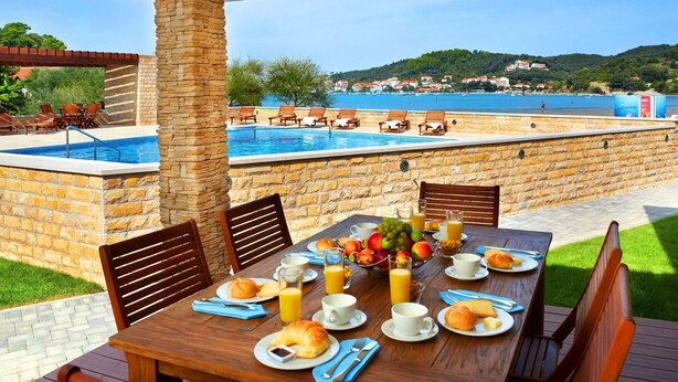 A dining table set with breakfast items and a view of a pool and beach.