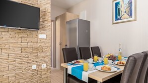 A dining area with a stone wall, a flat-screen TV, a refrigerator, and a table set for breakfast with plates, glasses, and a bottle.