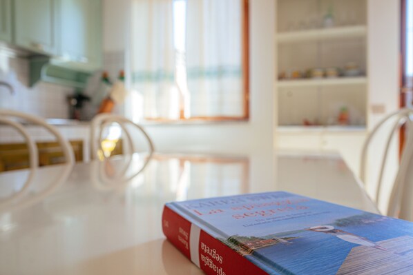 A book on a table in a room with a window and a kitchen in the background.
