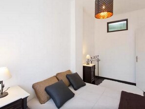 A hotel room with a bed, pillows, a bedside table, a lamp, a hanging light fixture, and a framed picture on the wall. - Sunny Apartment In City Center (Porto)
