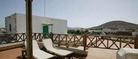 A rooftop terrace with two lounge chairs, a small building with a green door, and a mountain in the background.