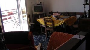 A dining area with a table covered by a yellow tablecloth, chairs, and a television on a stand.