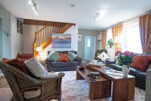 A living room with a staircase, two sofas, a coffee table, and a vase of flowers. - Stables Retreat - Direct Access to The Forest (Burley)