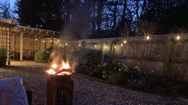 A fire pit with flames, surrounded by gravel and plants, under a wooden pergola with string lights. - Stables Retreat - Direct Access to The Forest (Burley)