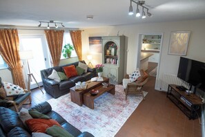 A living room with a sofa, coffee table, and a television. There is a bookshelf and a plant in the room. - Stables Retreat - Direct Access to The Forest (Burley)
