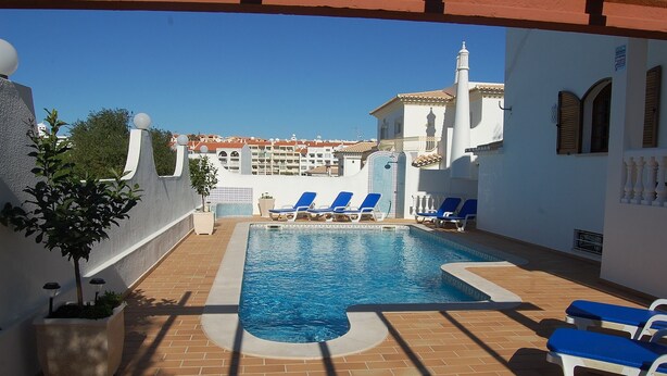 A swimming pool with blue lounge chairs, a tiled deck, and a building with a white facade in the background. - Large Villa in a relaxing area, with a private Pool and great Sea view. (Forte de São João)