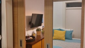 A bedroom with a bed, a bedside table, a TV, and a window. - Vintage Apartment in Anjos, Central Lisbon (Lisboa)